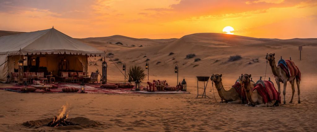 Dubai Desert Safari Guide: Morning vs Evening vs Overnight — Which One Fits Your Trip? 2 A desert camel camp among sand dunes at sunset in the UAE