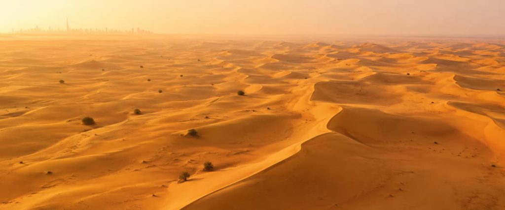 Best Time to Visit Dubai from India: A Season-by-Season Guide (2026) 2 Aerial view of golden sand dunes in the desert outside Dubai in summer heat